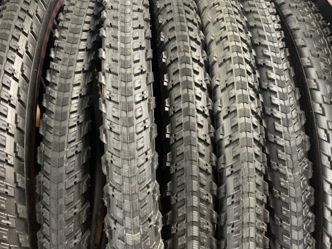A row of neatly arranged, textured bicycle tires with prominent tread patterns. The tires are displayed vertically, showcasing the intricate details of the rubber surface.