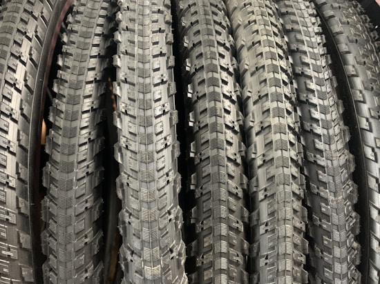 A row of neatly arranged, textured bicycle tires with prominent tread patterns. The tires are displayed vertically, showcasing the intricate details of the rubber surface.