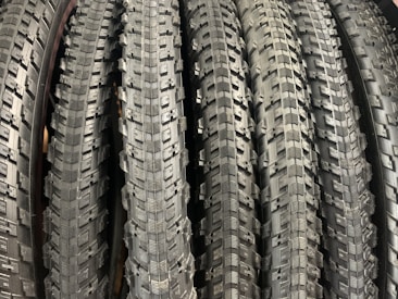 A row of neatly arranged, textured bicycle tires with prominent tread patterns. The tires are displayed vertically, showcasing the intricate details of the rubber surface.