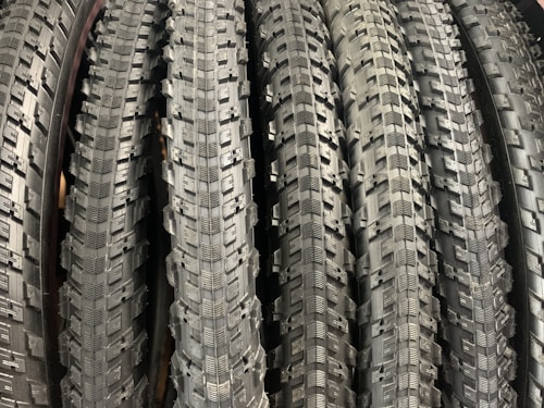 A row of neatly arranged, textured bicycle tires with prominent tread patterns. The tires are displayed vertically, showcasing the intricate details of the rubber surface.