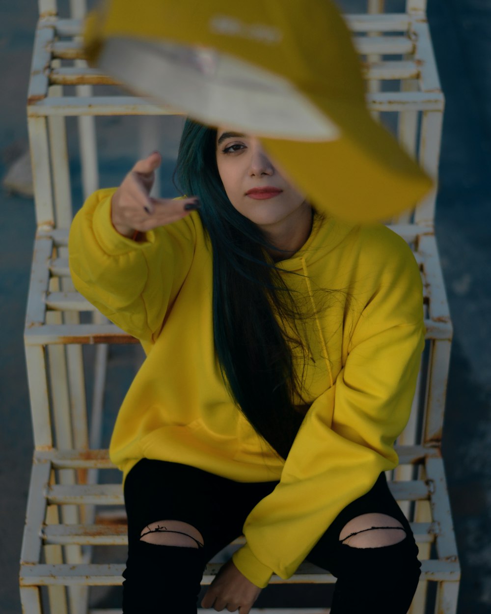 woman in yellow pullover hoodie sitting on brown wooden steps throwing yellow cap