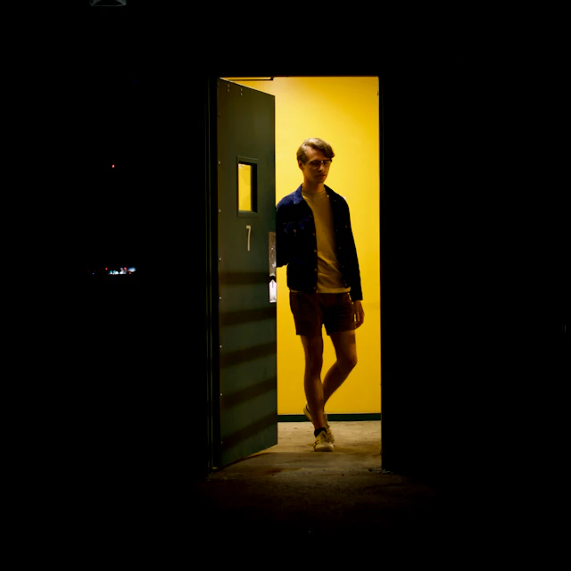 A person in denim shorts and sneakers standing in a doorway of a parking deck at night
