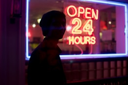 man standing beside open 24 hours signage during nighttime