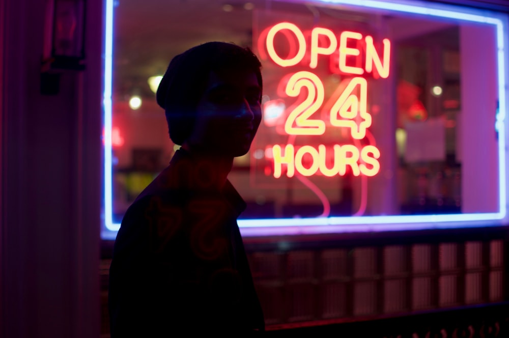 homem em pé ao lado de sinalização aberta 24 horas durante a noite