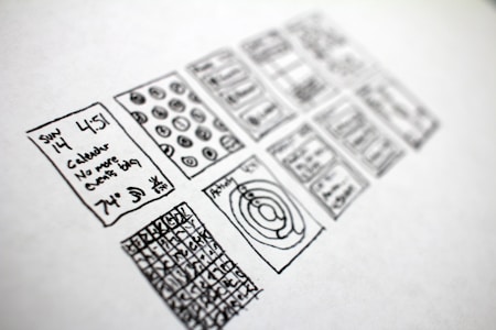 A series of hand-drawn sketches on a piece of paper, featuring various rectangles filled with doodles. The sketches include a calendar with written text indicating a specific date and time, abstract diagrams, and grid patterns with numbers or symbols.