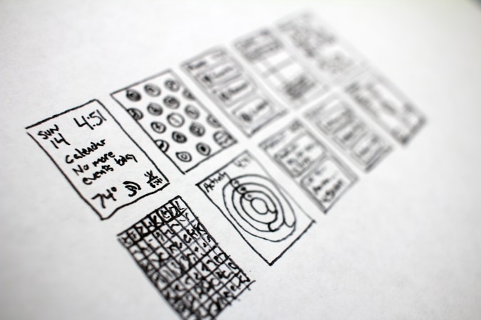 A series of hand-drawn sketches on a piece of paper, featuring various rectangles filled with doodles. The sketches include a calendar with written text indicating a specific date and time, abstract diagrams, and grid patterns with numbers or symbols.
