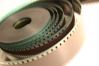 A close-up view of a coiled strip of film, with visible perforations along its edges and a slight metallic sheen. The film is tightly wound in concentric circles, creating a layered visual effect.