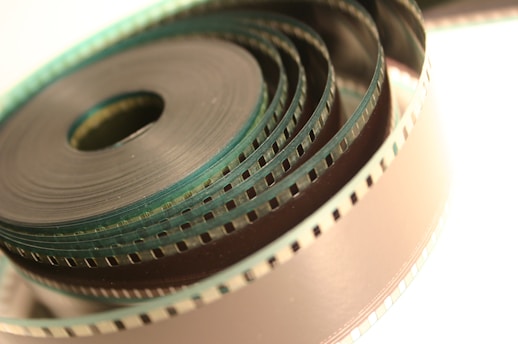 A close-up view of a coiled strip of film, with visible perforations along its edges and a slight metallic sheen. The film is tightly wound in concentric circles, creating a layered visual effect.