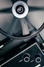A close-up view of a film projector with a rotating reel. The image captures the mechanical components, including knobs labeled 'Framer' and 'Focus' and a visible part of the reel mid-spin.