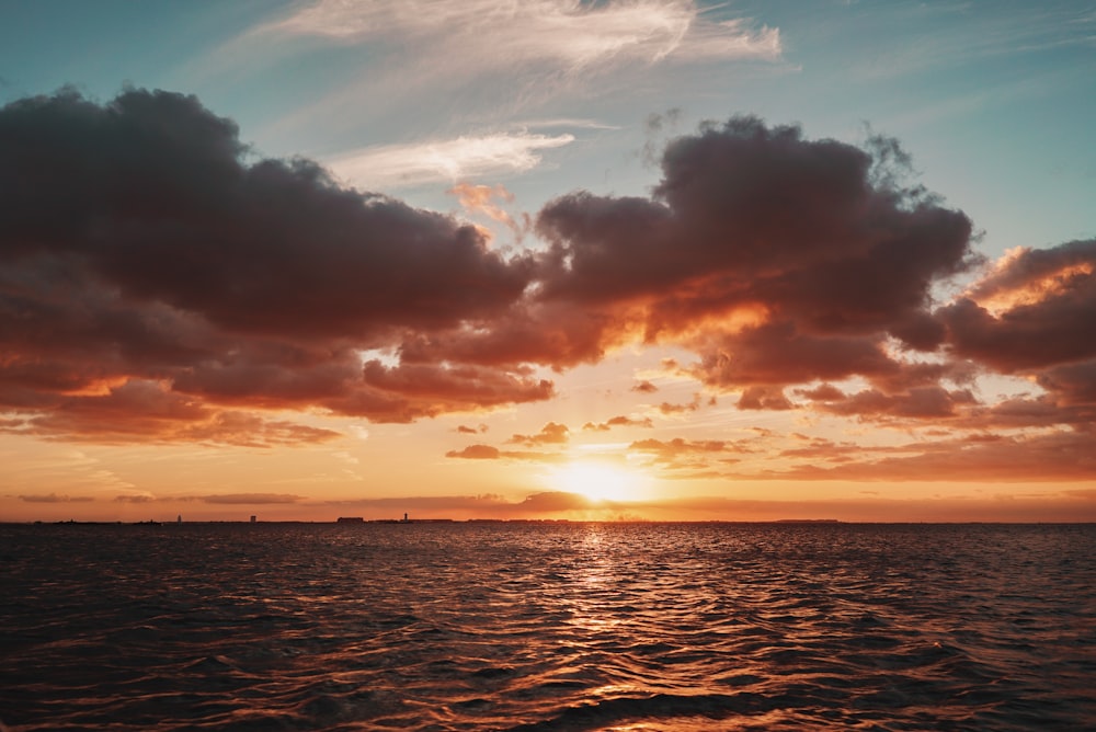 silhouette photography of the sea under a cloudy sky during golden hour