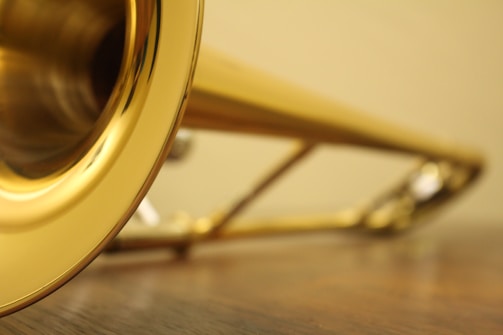 A close-up view of a brass trumpet laid on a wooden surface with focus on the bell of the instrument, displaying its shiny, reflective surface.