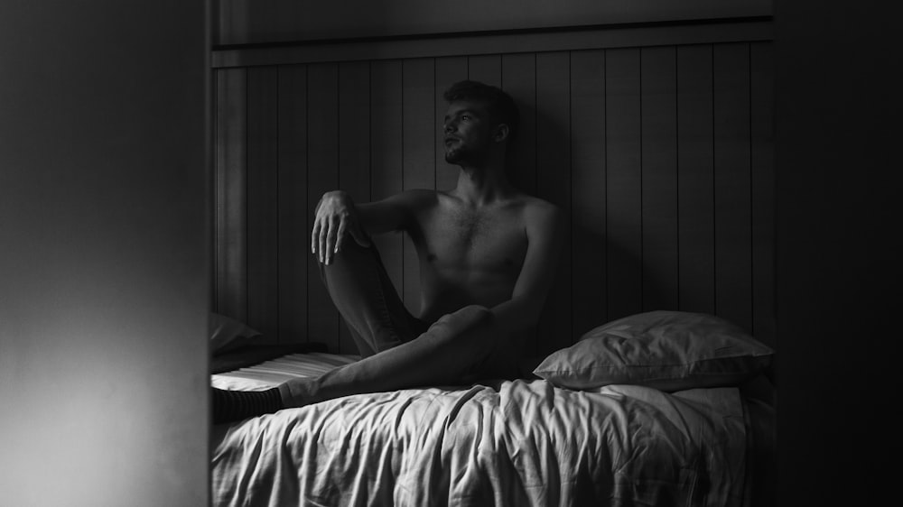 greyscale photography of man sitting on bed