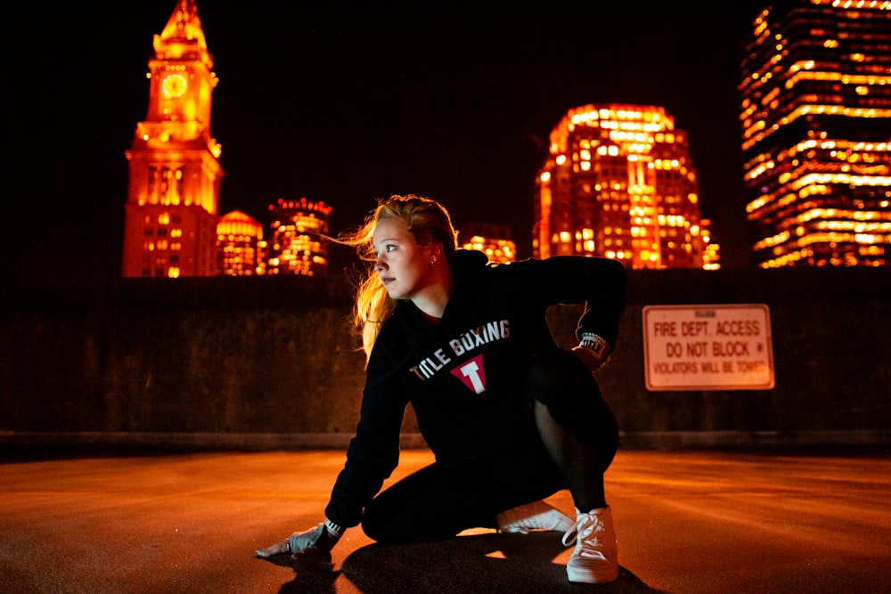 woman in black hoodie jacket crouching near wall during daytime