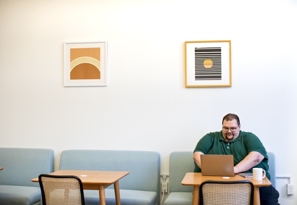 man in green polo shirt sitting on sofa near table while using laptop computer inside room