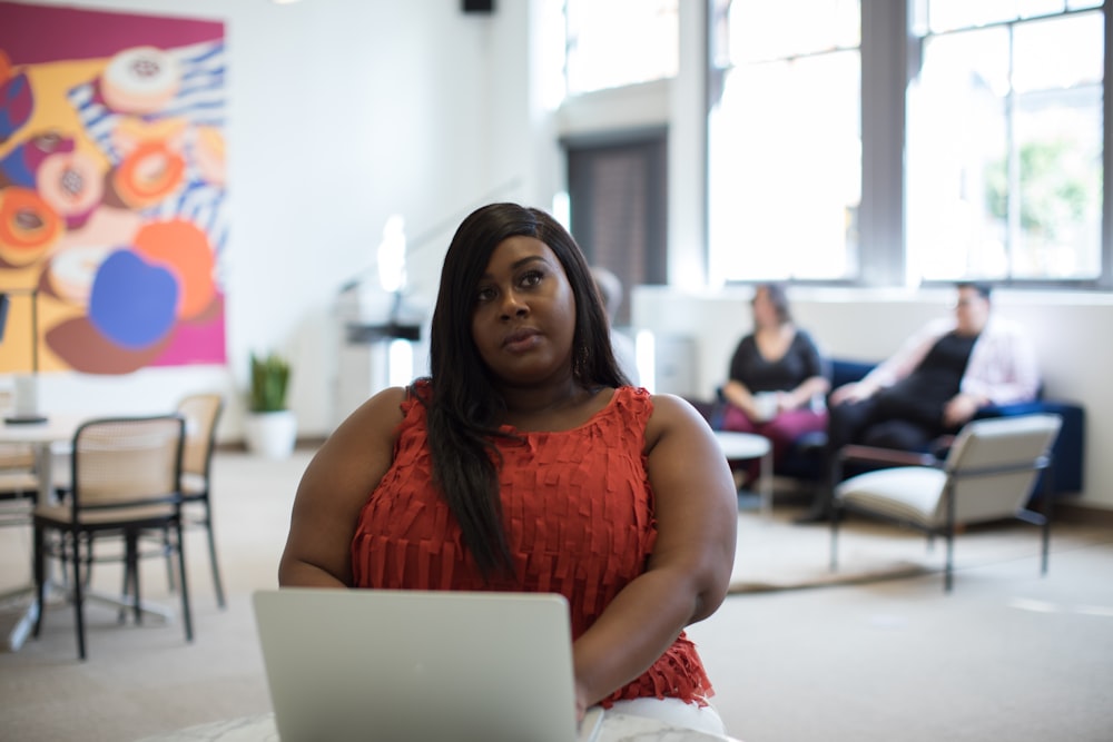 woman in orange sleeveless top using laptop computer inside building