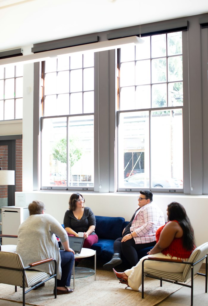 Four people talking in a bright room with tall windows
