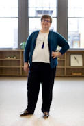A smiling individual standing confidently in a tidy, sunlit room.