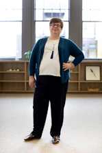 A confident person smiling, standing tall with a calm, assured expression in a sunlit room.