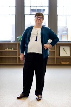 A smiling individual standing confidently in a tidy, sunlit room.