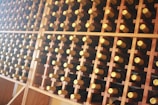 A well-organized wine rack filled with numerous bottles of wine. The bottles are stored horizontally, showcasing their gold foil tops. The rack is made of wooden compartments arranged in a grid pattern.