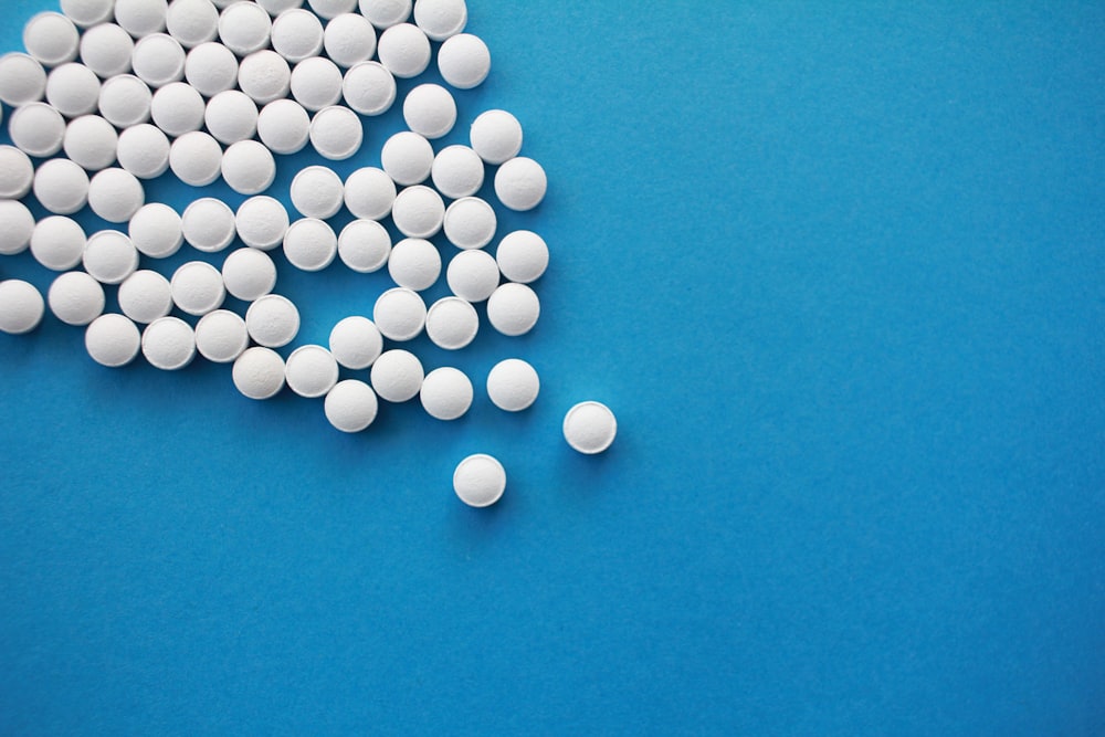 Un montón de píldoras blancas sentadas encima de una mesa azul