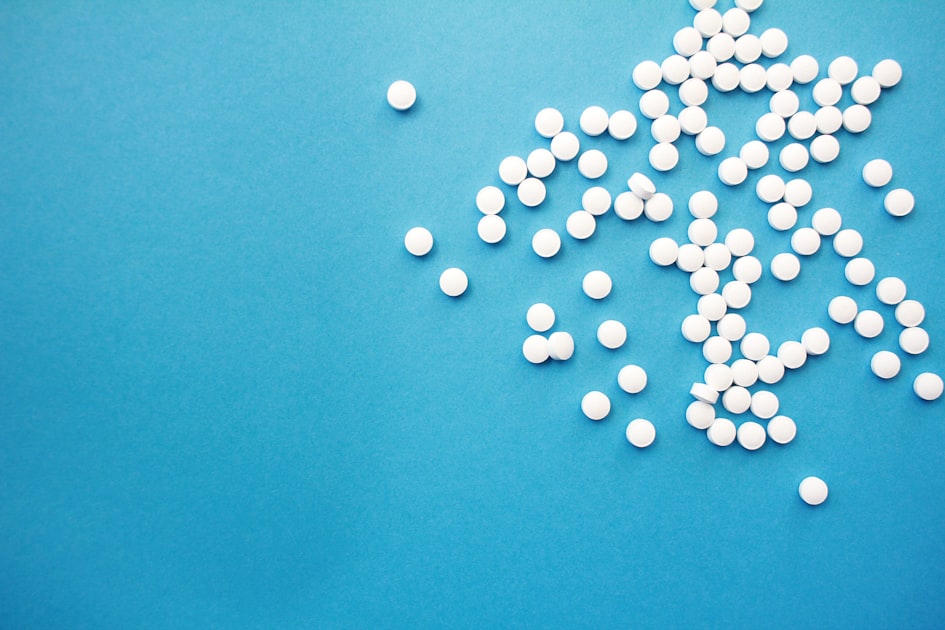 Witte ronde medicijntabletten verspreid over een blauw oppervlak als illustratie bij sildenafil doseringskeuze