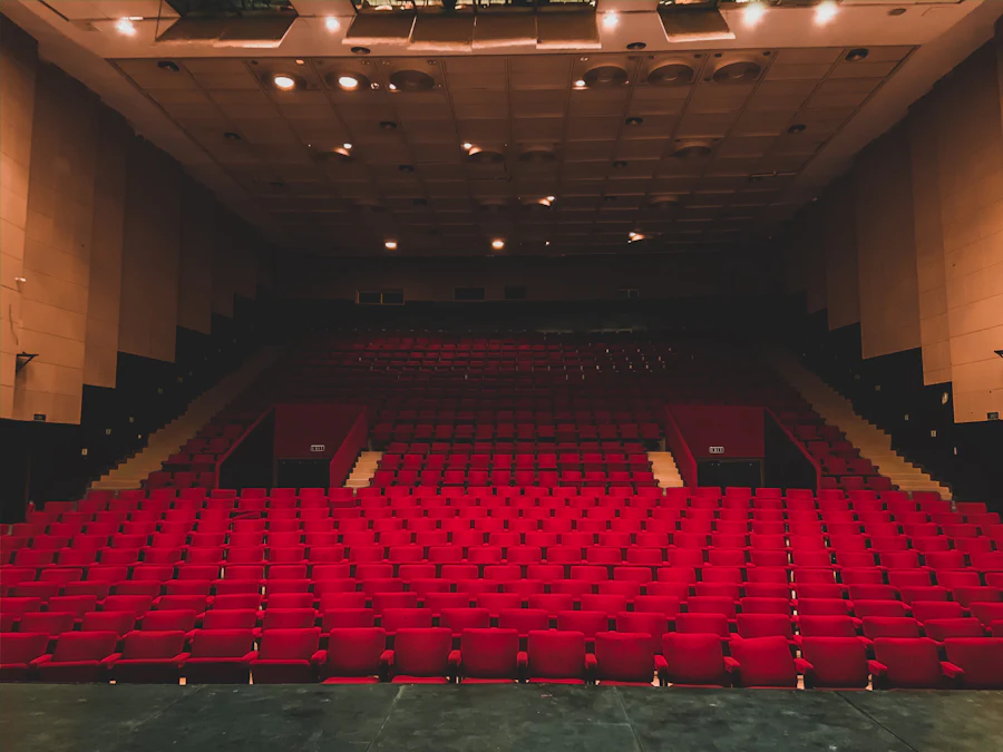 An empty auditorium of red seats raked towards a lit stage.