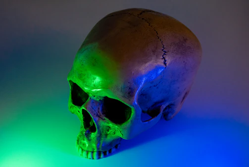 A massive cracked skull structure glows faint purple, its eye sockets burning with soft embers in a gothic surreal night.