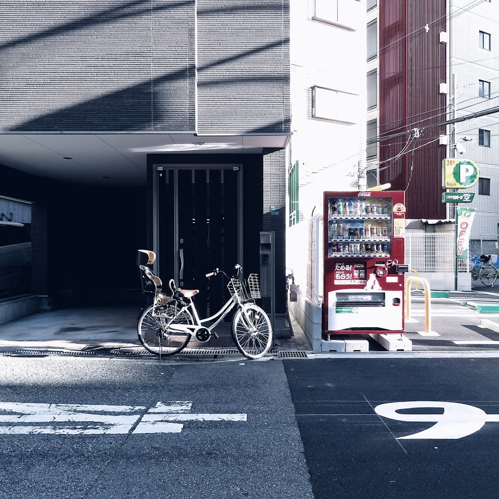 view photography of gray bicycle parked near building beside vending machine during daytime