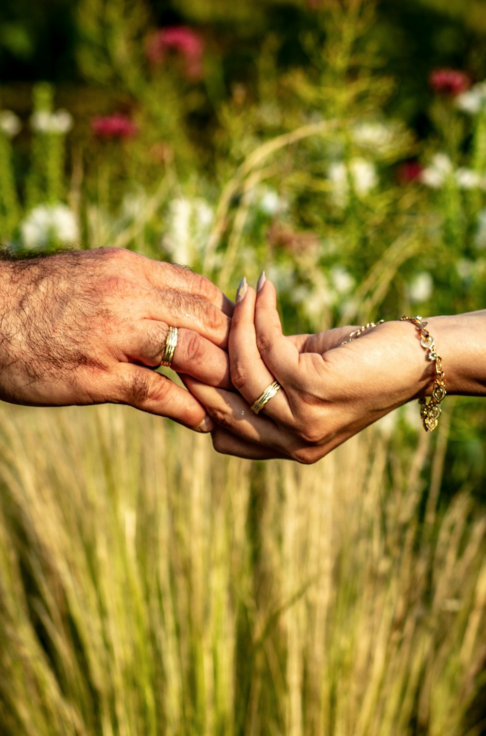 holdings hands with gold-colored ring over flower garden