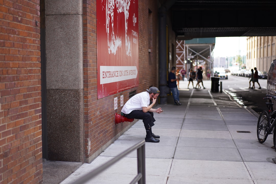 man sitting beside wall using smartphone