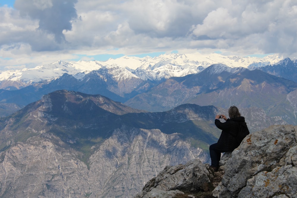 man sitting on cliff under white clouds