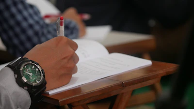 Close-up of a teacher's hands grading papers with colorful pens on a wooden desk