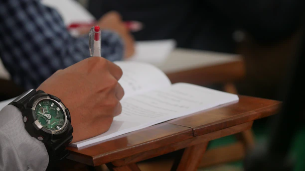 A close-up of hands editing a printed manuscript with a red pen on a wooden desk.