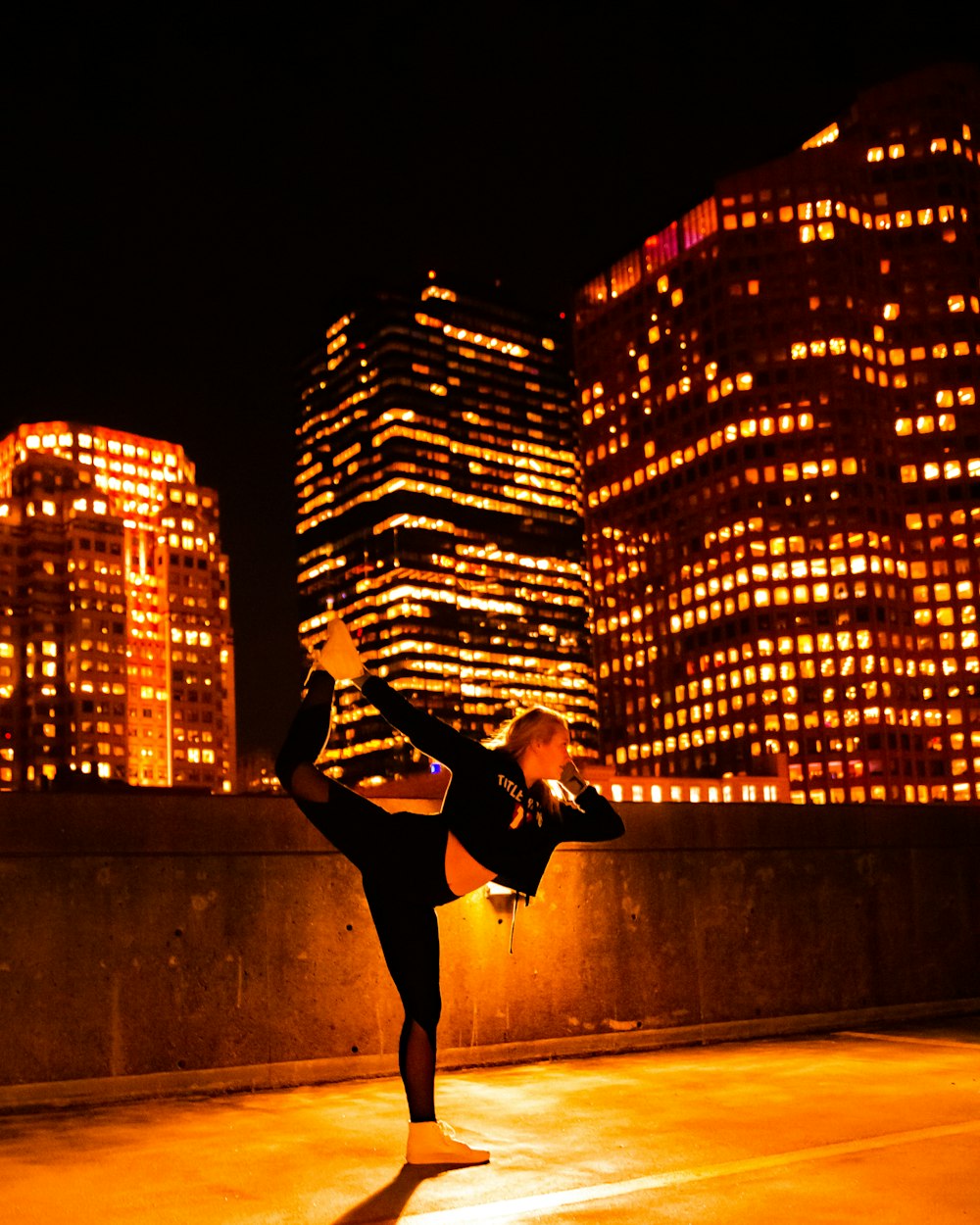 barefooted woman wearing black and white jacket dancing viewing high-rise buildings during night time