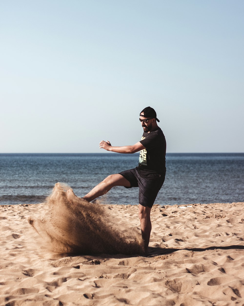 man kicking a sand beside seashore during daytime