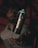 A spray paint can labeled 'BLACK' hovers over an open hand in a dimly lit setting, with a person blurred in the background.