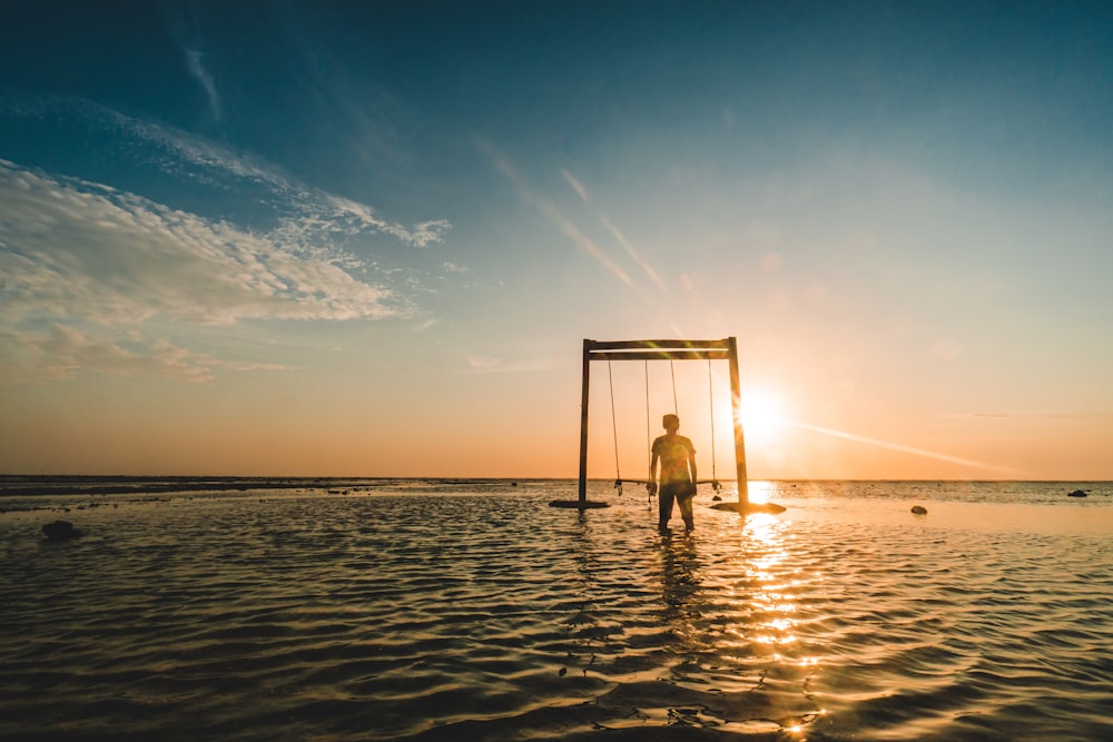 person standing near swing on body of water