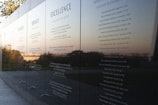 A polished black stone wall displays engraved text featuring principles such as Integrity, Service, and Excellence. The reflective surface captures a scenic view of trees and the horizon in the background, suggesting an outdoor memorial or monument.