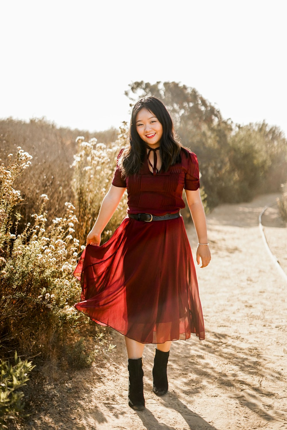 a woman in a red dress walking down a dirt road