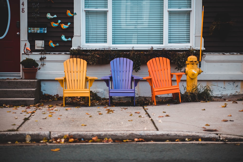 three Adirondack chairs with different colors outside a house