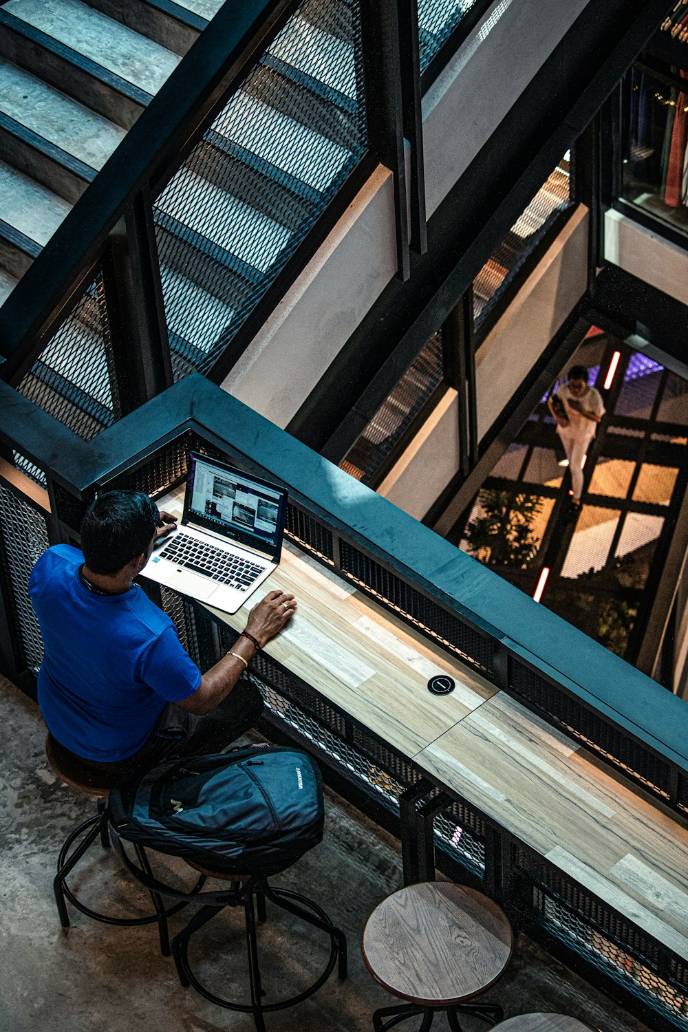 man in blue shirt sitting on chair near table using laptop computer inside building
