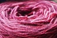 A close-up view of a ball of yarn in shades of pink and purple. The texture of the yarn fibers is clearly visible, showing intricately woven threads.