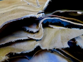 A close-up view of several overlapping sheets of beige and light brown leather with frayed edges. The texture of the leather is visible, with slight wrinkles and natural imperfections.
