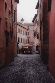 A cobblestone alley lined with vibrant cafes and blooming flowers in a Roman neighborhood.