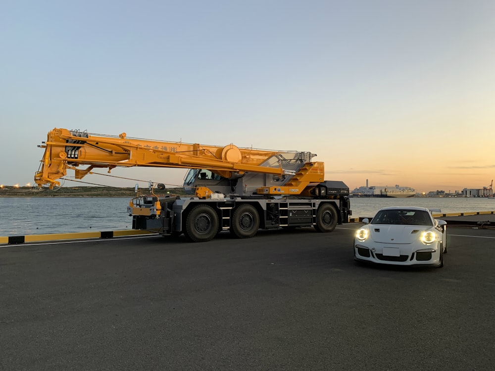white sports car near yellow and black heavy equipment during daytime