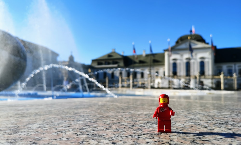 mini figura rossa e gialla sulla superficie di marmo vicino alla fontana d'acqua