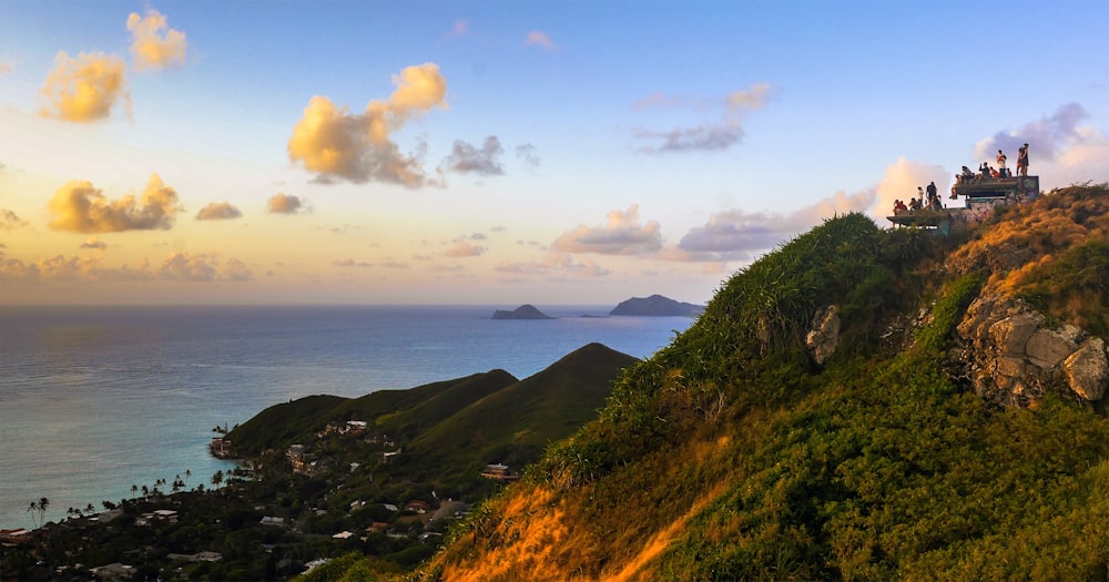 house on cliff viewing mountain and body of water under blue and yellow sky