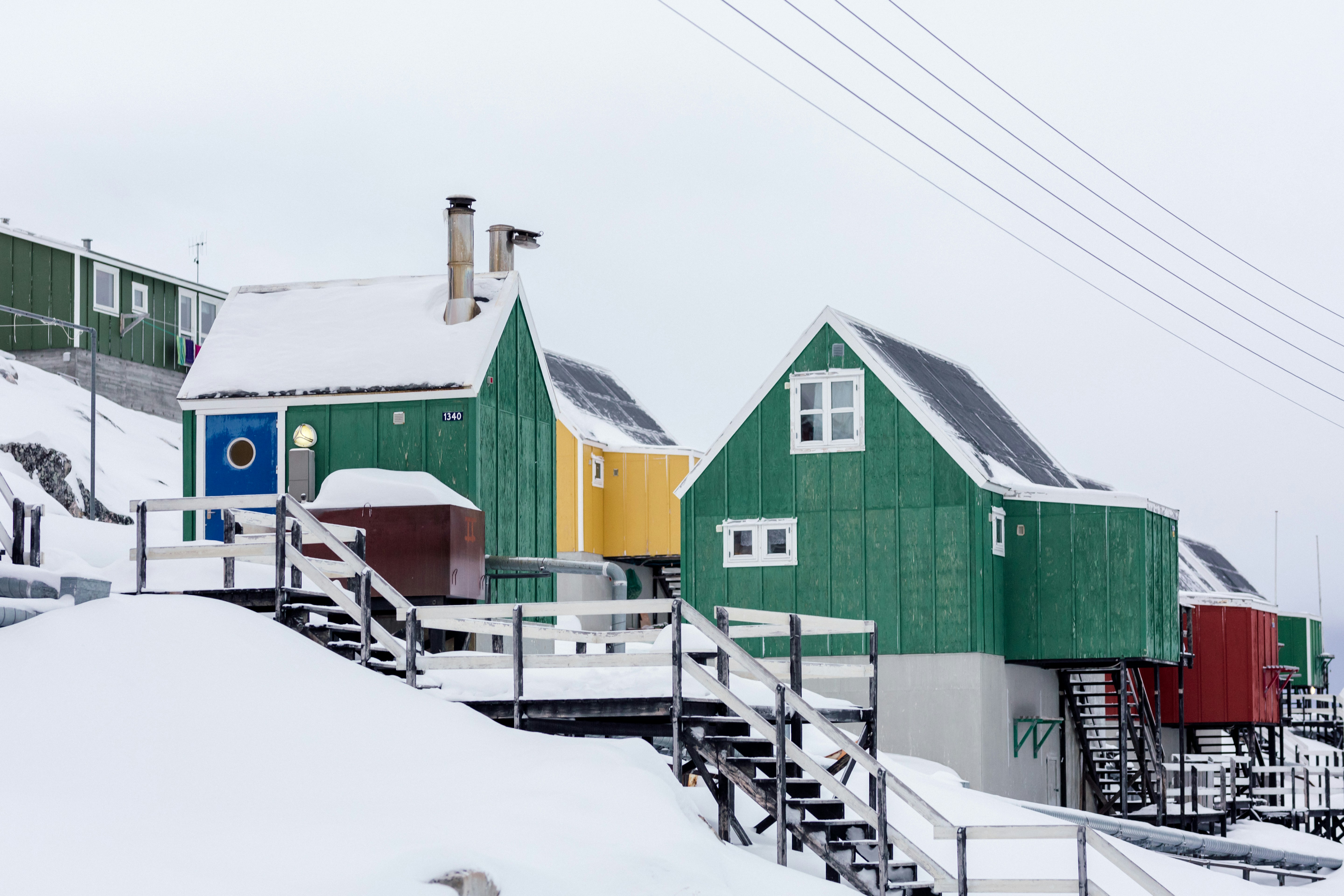 maisons en bois vert sur une pente enneigée sous un ciel blanc
