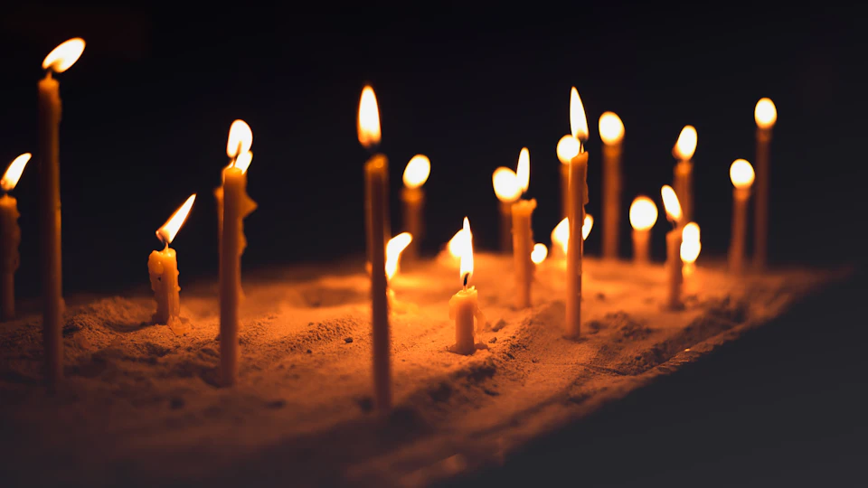 The image shows a group of candles arranged on a wooden surface, with their flames dancing and casting a warm glow. The candles are lit from both sides, creating a symmetrical pattern that draws the eye towards them. The background is dark, allowing the candles to stand out prominently against it.